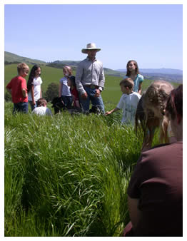 Joe and children in knee deep grass on Spring Field Day 